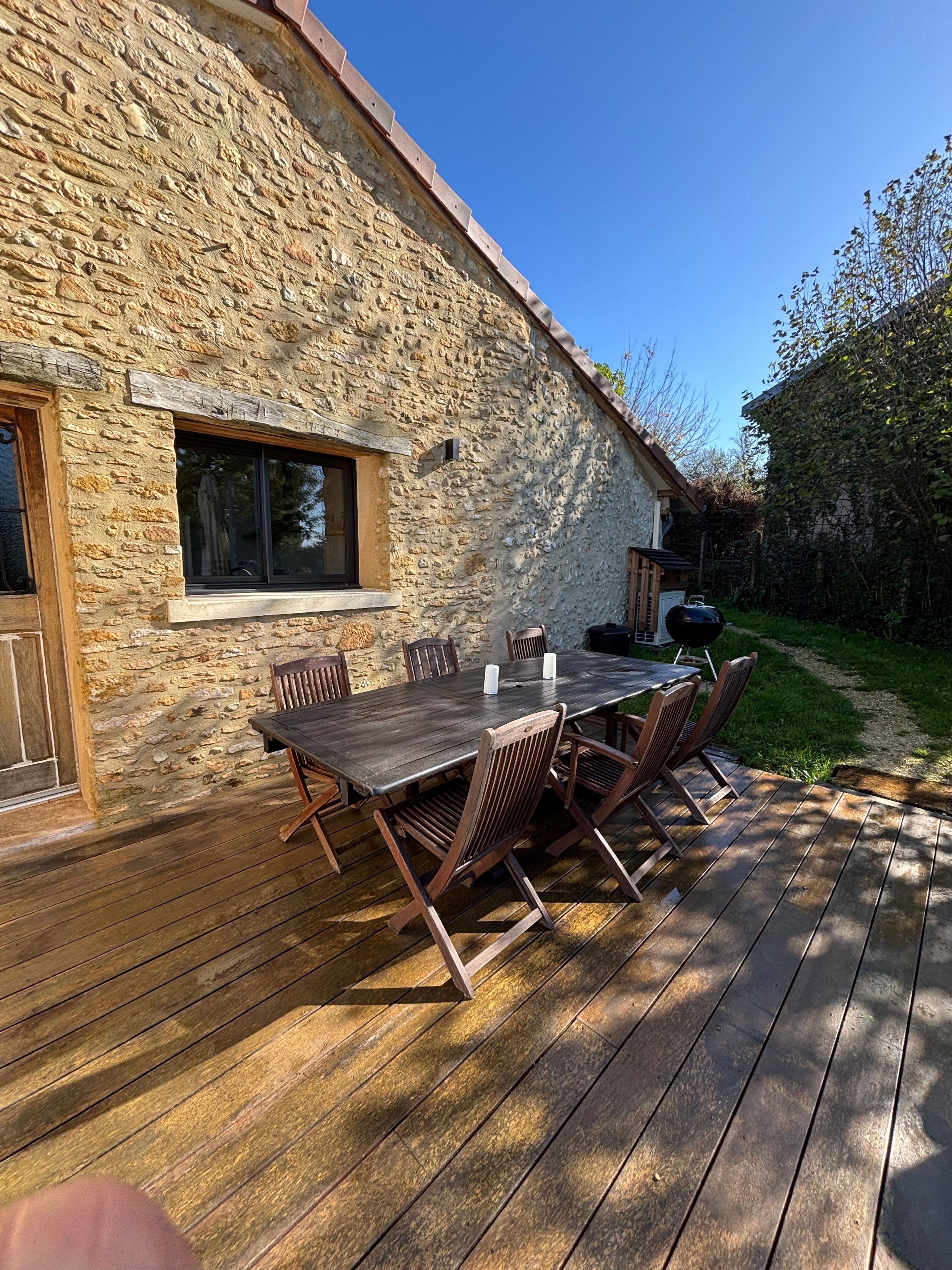 Ein Steinhaus mit einer Holzterrasse und einem Tisch mit Stühlen.