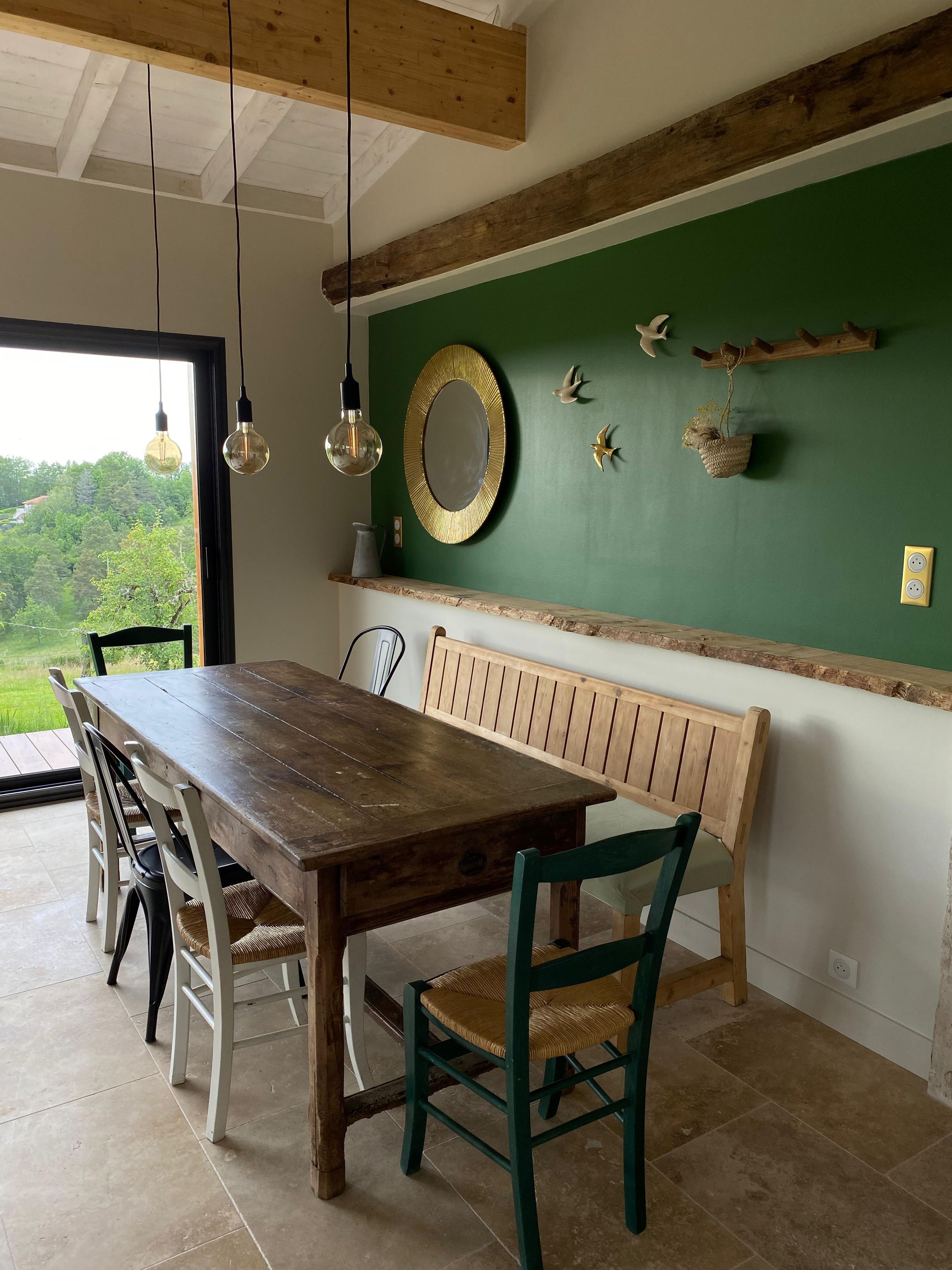 Een eetgedeelte met een houten tafel en stoelen, een bankje en een groene wand met decoratieve objecten.