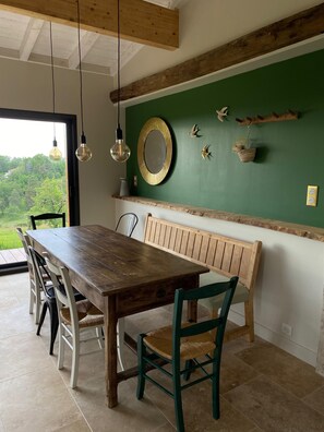 Un espace repas comprenant une table et des chaises en bois, un banc et un mur vert agrémenté d’objets décoratifs.