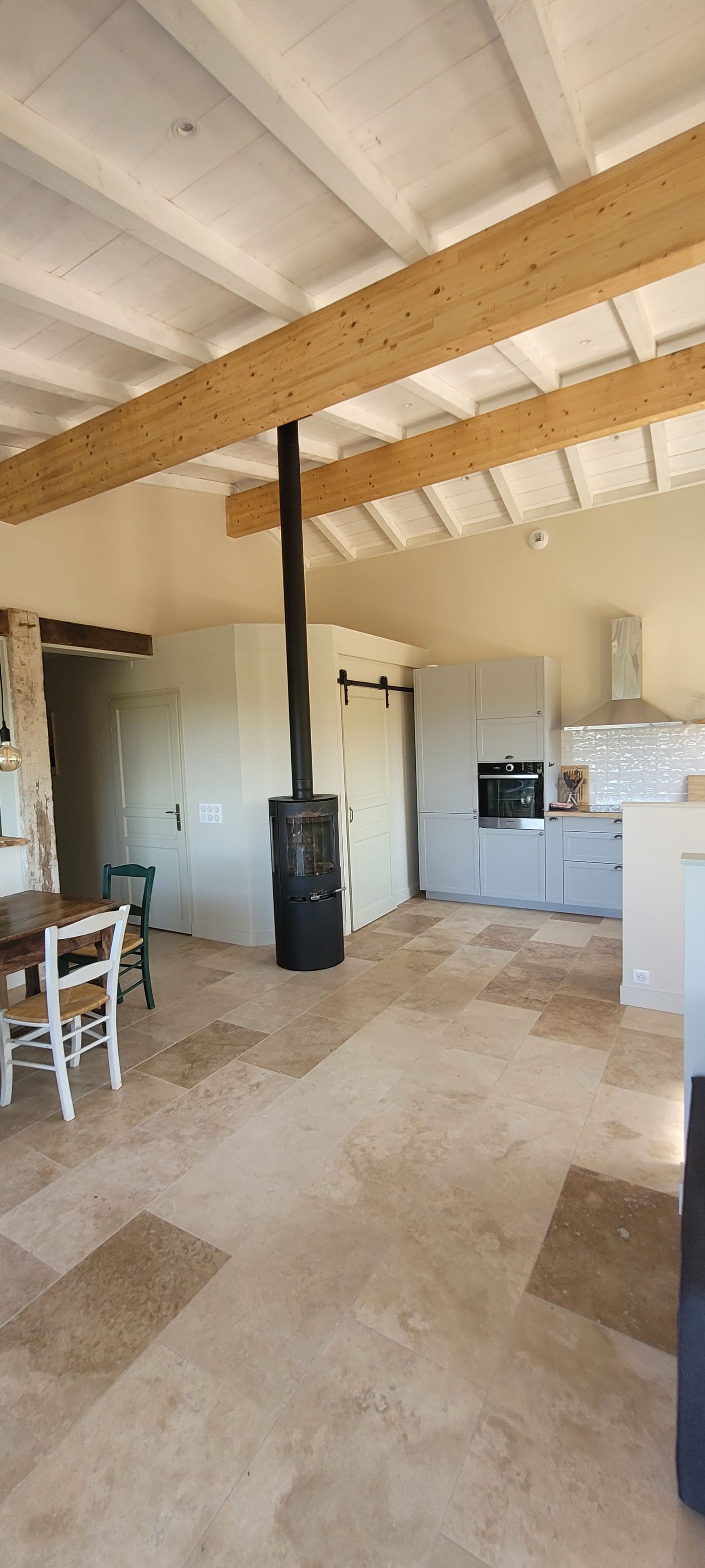 A spacious kitchen with a central chimney, white cabinets, and a dining area with a wooden table and chairs.