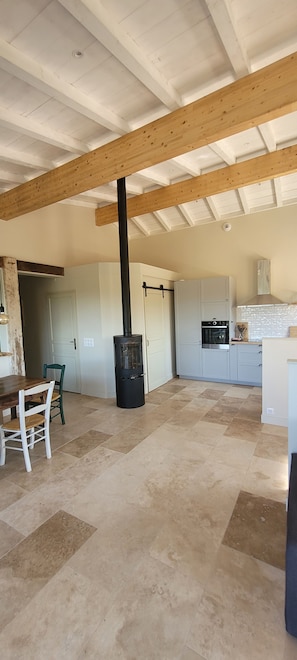 Una cocina amplia con chimenea central, armarios blancos y un comedor con mesa y sillas de madera.