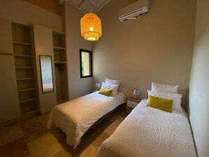 Un dormitorio con dos camas, un armario, una ventana y un equipo de aire acondicionado.