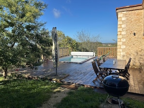 Patio trasero con piscina, mobiliario exterior y una parrilla.