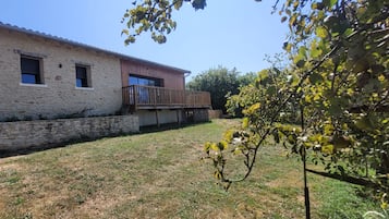 Un edificio de piedra con un balcón de madera, un muro de piedra y un patio cubierto de césped.