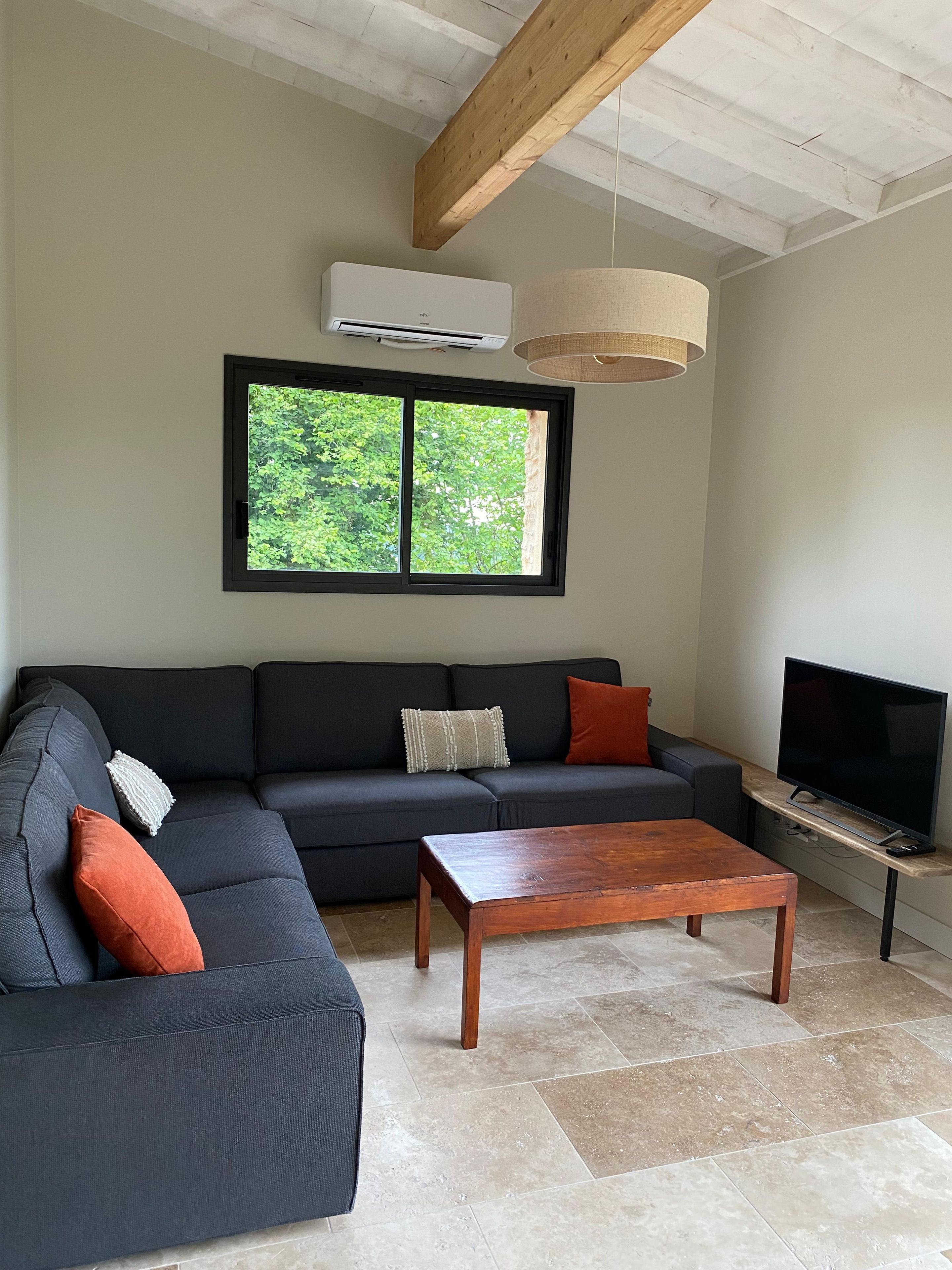 A living room with a sectional sofa, a coffee table, a television, and a window with a view of greenery.