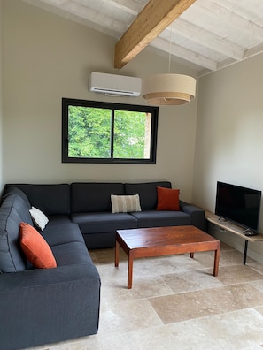 Un salón con un sofá modular, una mesa de centro, un televisor y una ventana con vistas al verdor.