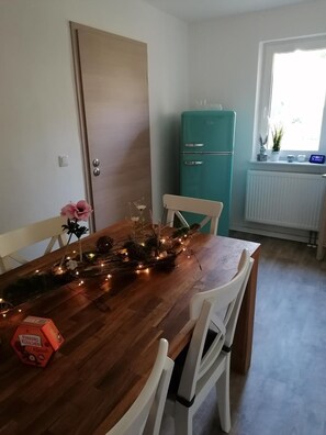 A dining area with a wooden table, white chairs, a teal refrigerator, and a window with a view.