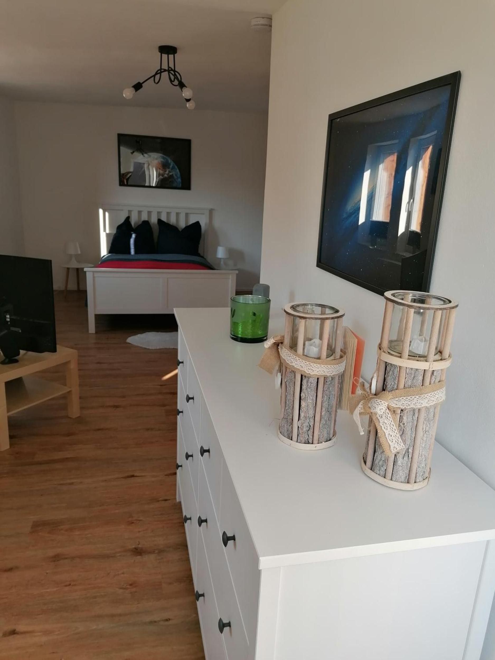 Ein stilvolles Wohnzimmer mit einem weißen Sofa, einem Fernseher und dekorativen Laternen auf einem weißen Konsolentisch.