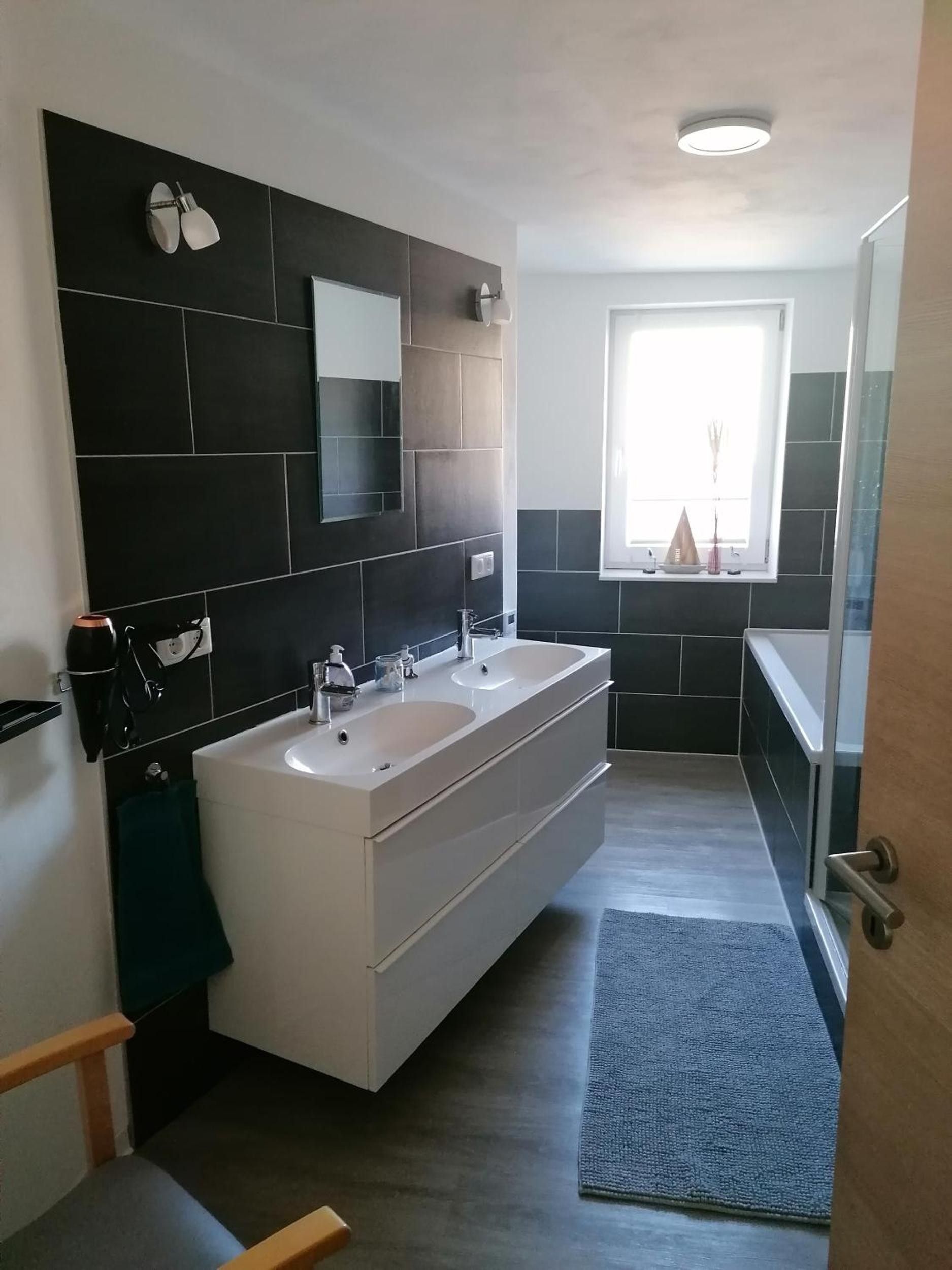 Ein modernes Badezimmer mit einem Doppelwaschtisch, einem großen Spiegel und einem Fenster für natürliches Licht.