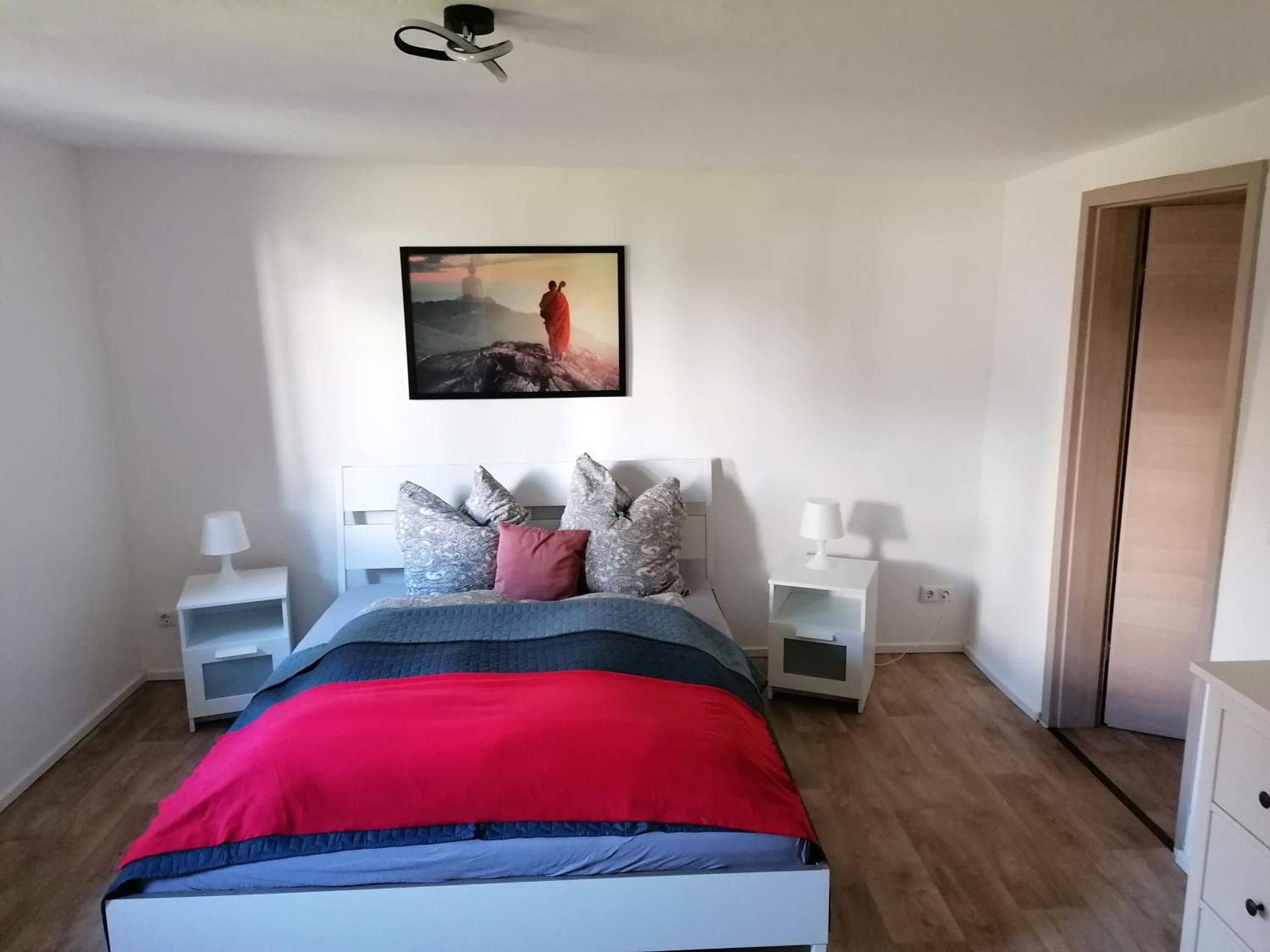 Ein Schlafzimmer mit einem Bett, Nachttischen, einem Wandbild und einer Tür.