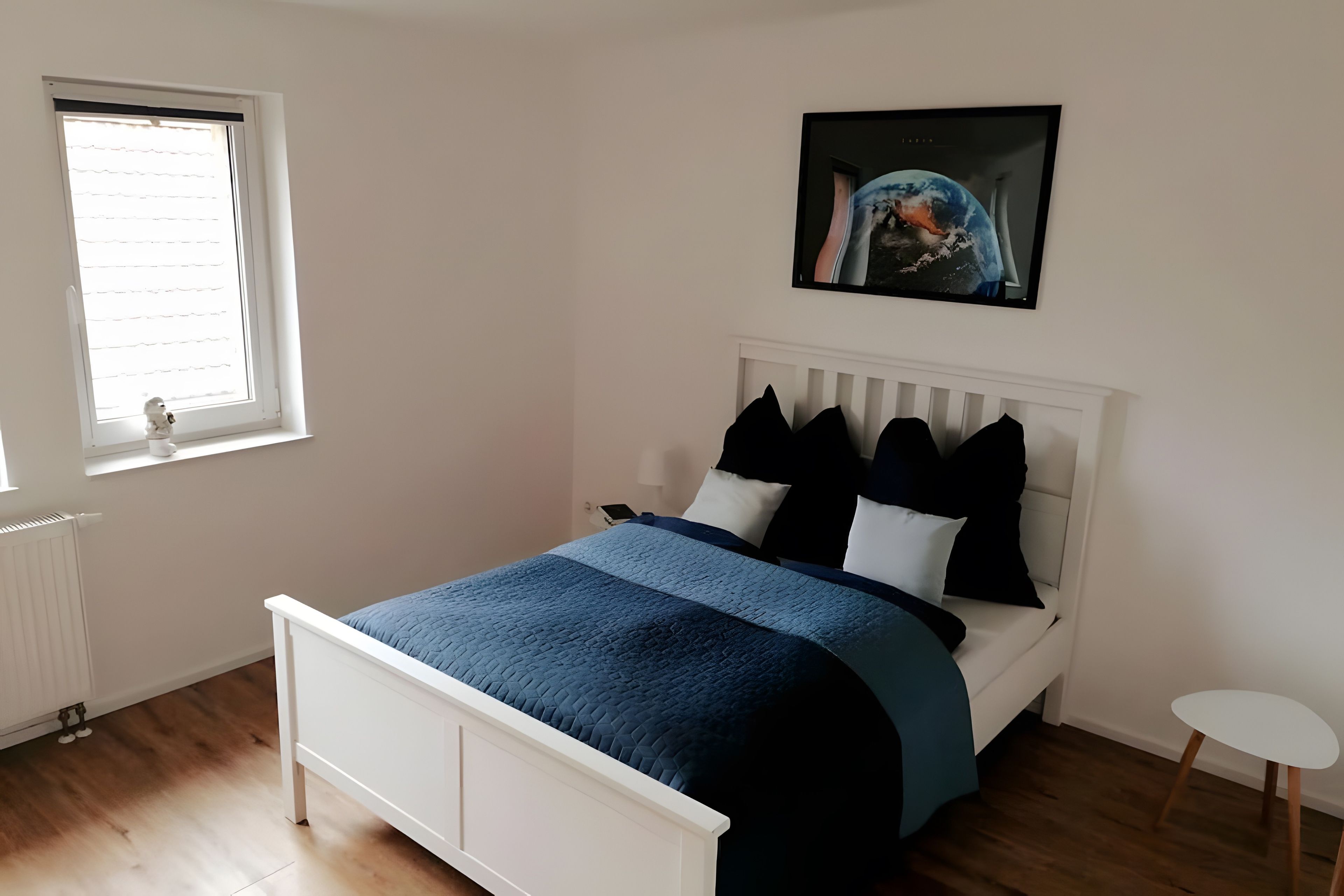Ein Schlafzimmer mit einem Bett, einem Fenster, einer Heizung und einem Bild an der Wand.