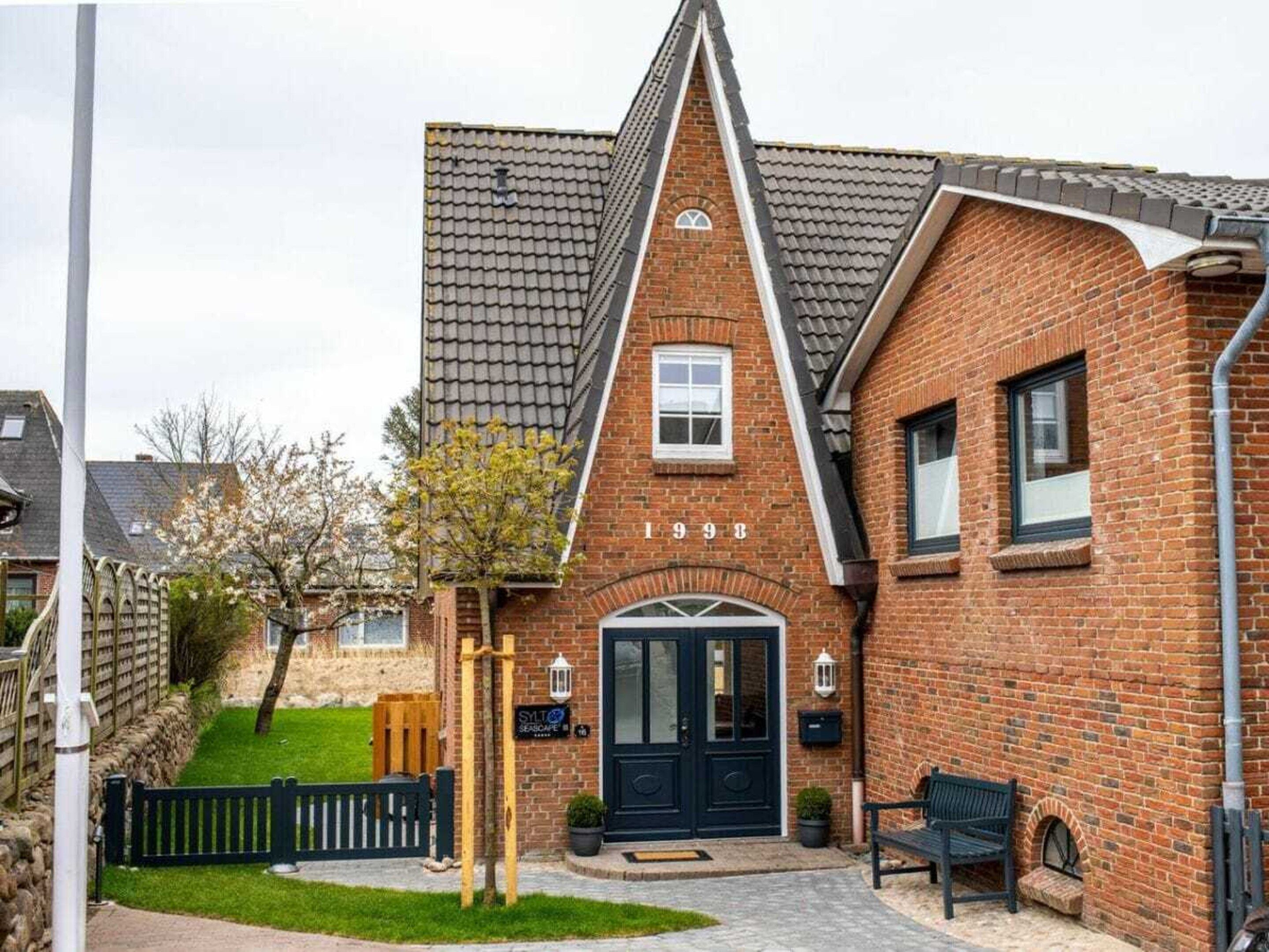 Ein Ziegelhaus mit schwarzer Haustür, einem kleinen Fenster und einem Jahrzeichen.