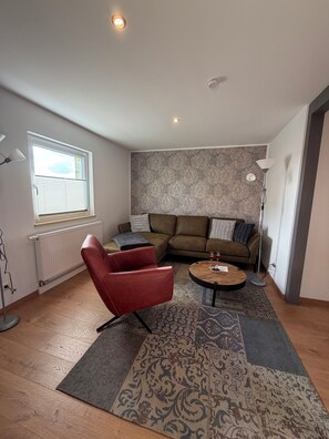 A living room with a red chair, a sofa, a coffee table, and a patterned rug.