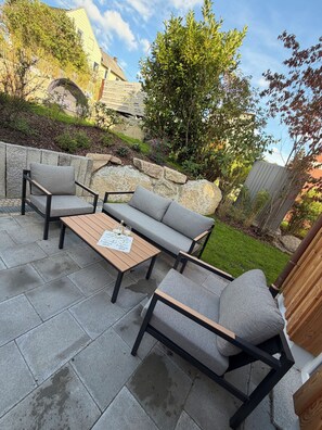 An outdoor patio with a sofa set, a wooden table, and a stone wall.
