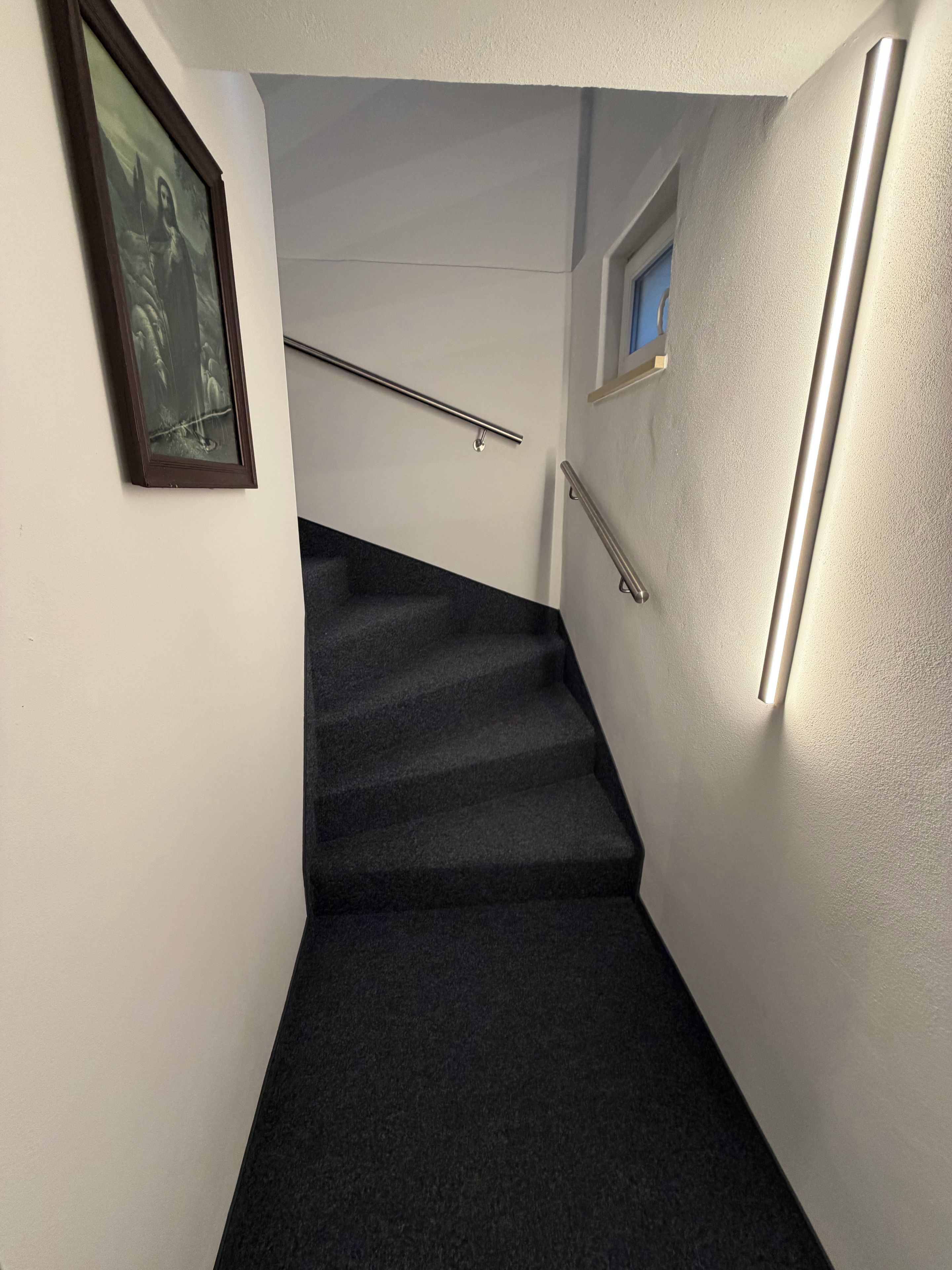 Una escalera con barandilla, un cuadro en la pared y una lámpara.