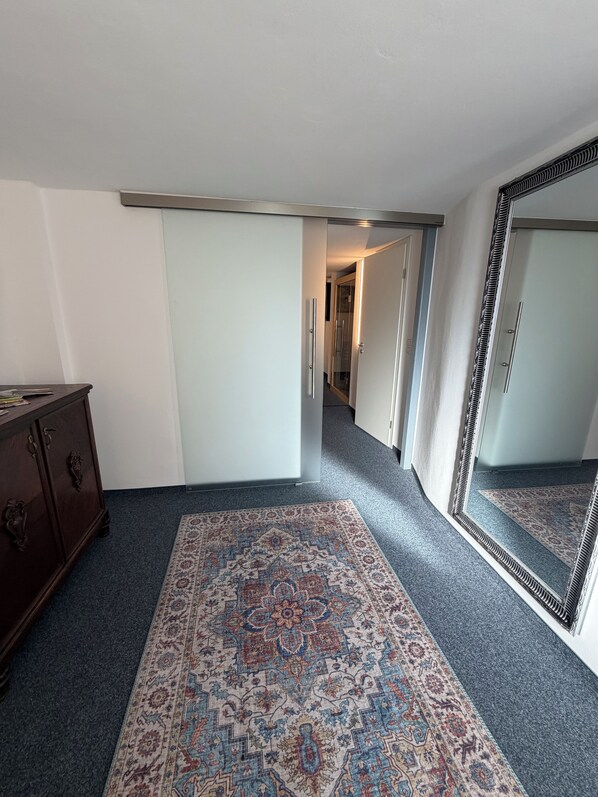 A hallway with a patterned carpet, a dresser, and a large mirror.