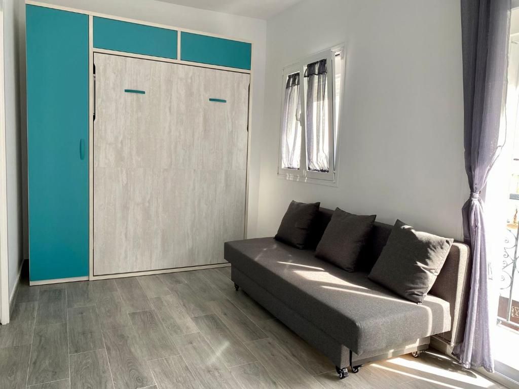 A room with a grey sofa, teal-colored wardrobe, and a window with curtains.