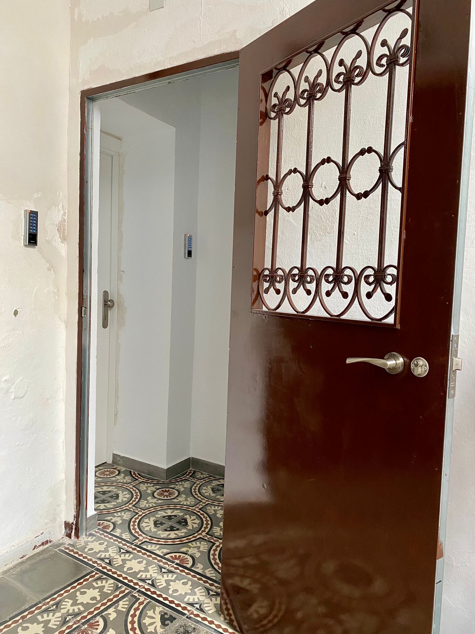 A room with a patterned floor, a door with a metal security gate, and a white wall with a light switch.