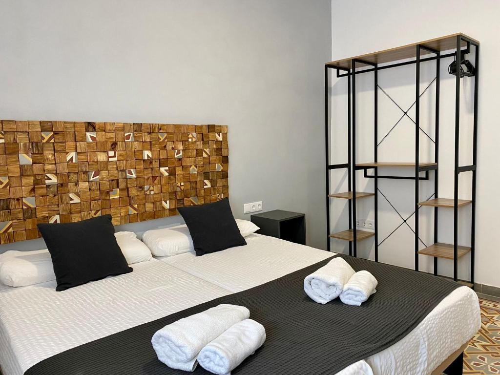 A hotel room with a bed, a headboard with a geometric pattern, a black metal shelf unit, and a patterned floor.