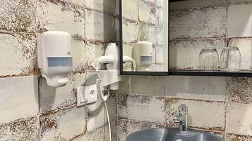A bathroom with a rustic tiled wall, a wooden sink, a mirror, and a hand dryer.