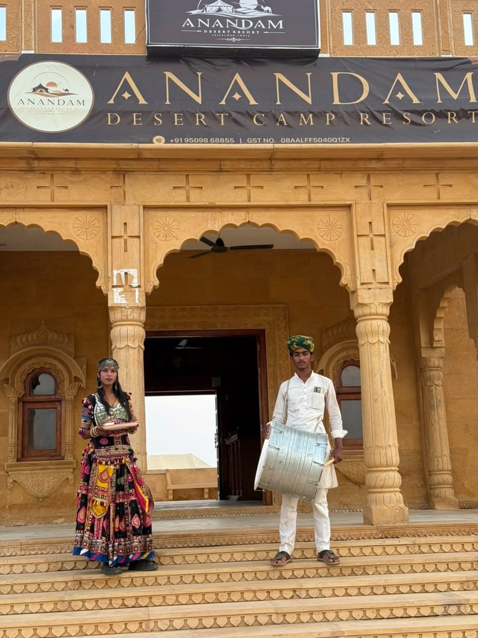 A building with a sign reading 'Anandam Desert Camp Resort' and a contact number.