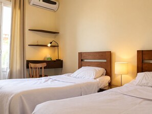 Et hotelværelse med to senge, et skrivebord med stol, en lampe og et klimaanlæg.