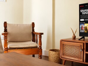 A wooden chair with a cushion, a television displaying a Netflix series, and a wicker basket. - Charming 2BR in Downtown Near Egyptian Museum (Cairo Governorate)