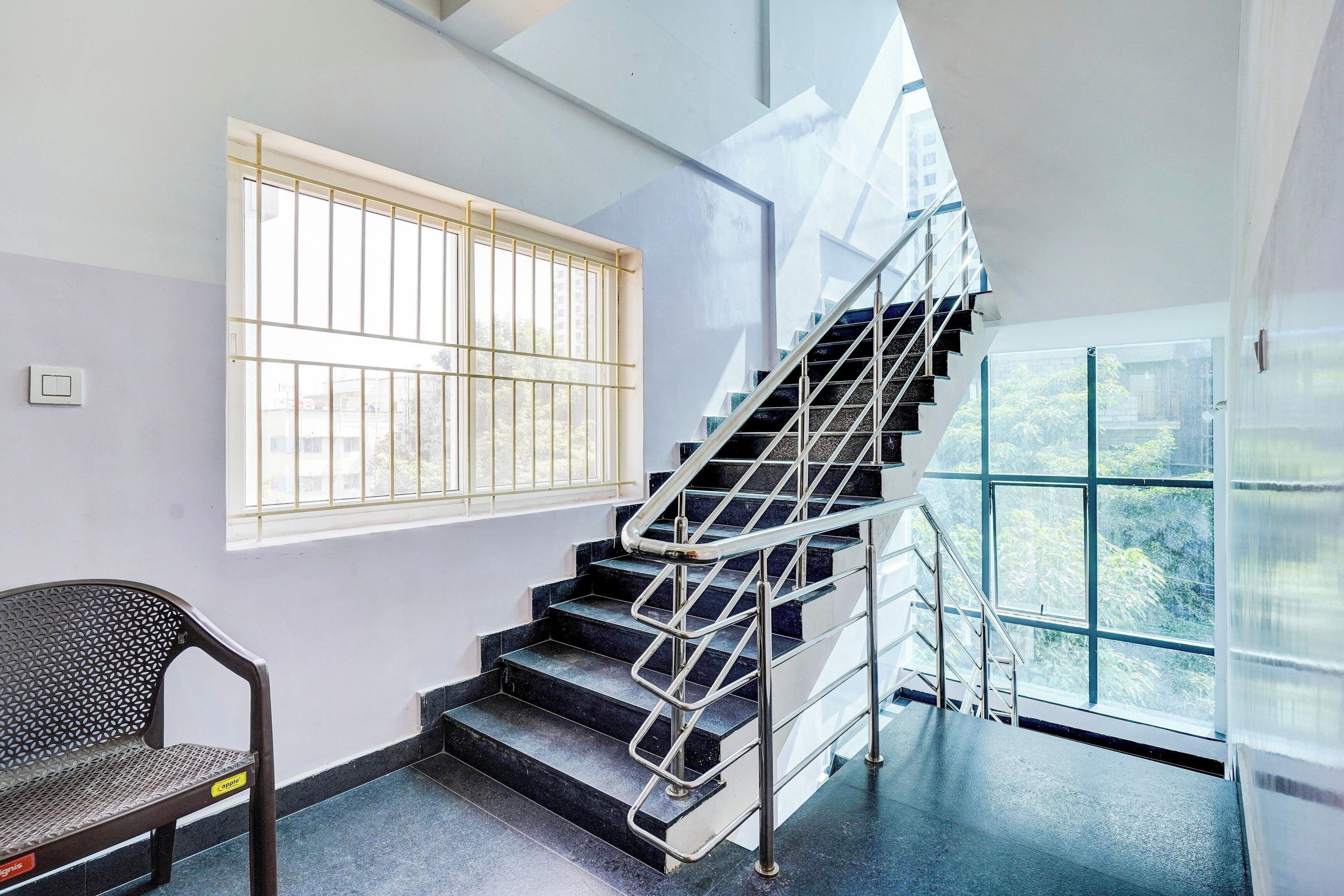 A staircase with metal railings, a chair, and a window with bars.