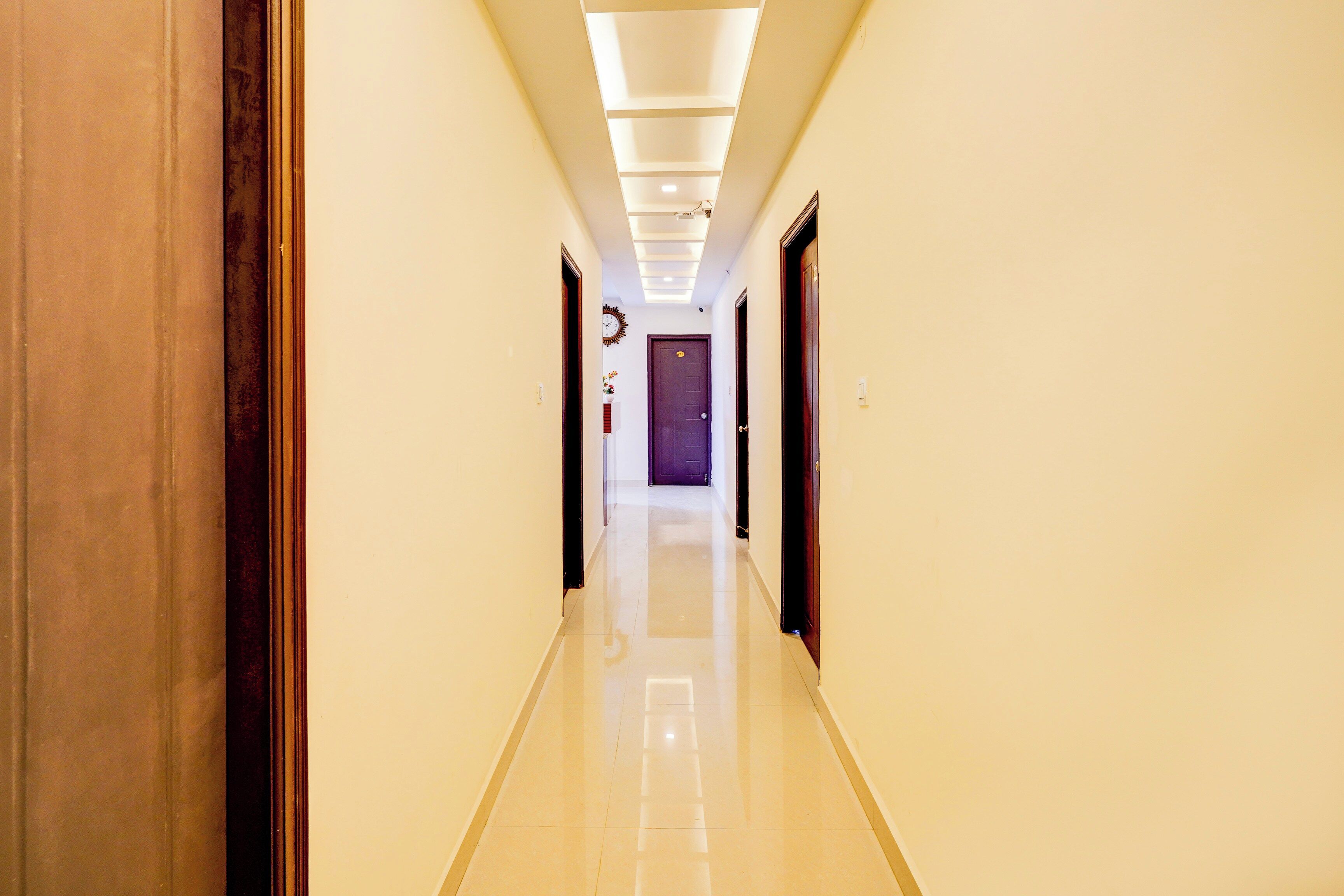 A hotel corridor with a tiled floor, wooden doors, and a ceiling with recessed lighting.