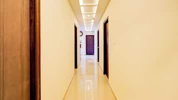 A hotel corridor with a tiled floor, wooden doors, and a ceiling with recessed lighting.
