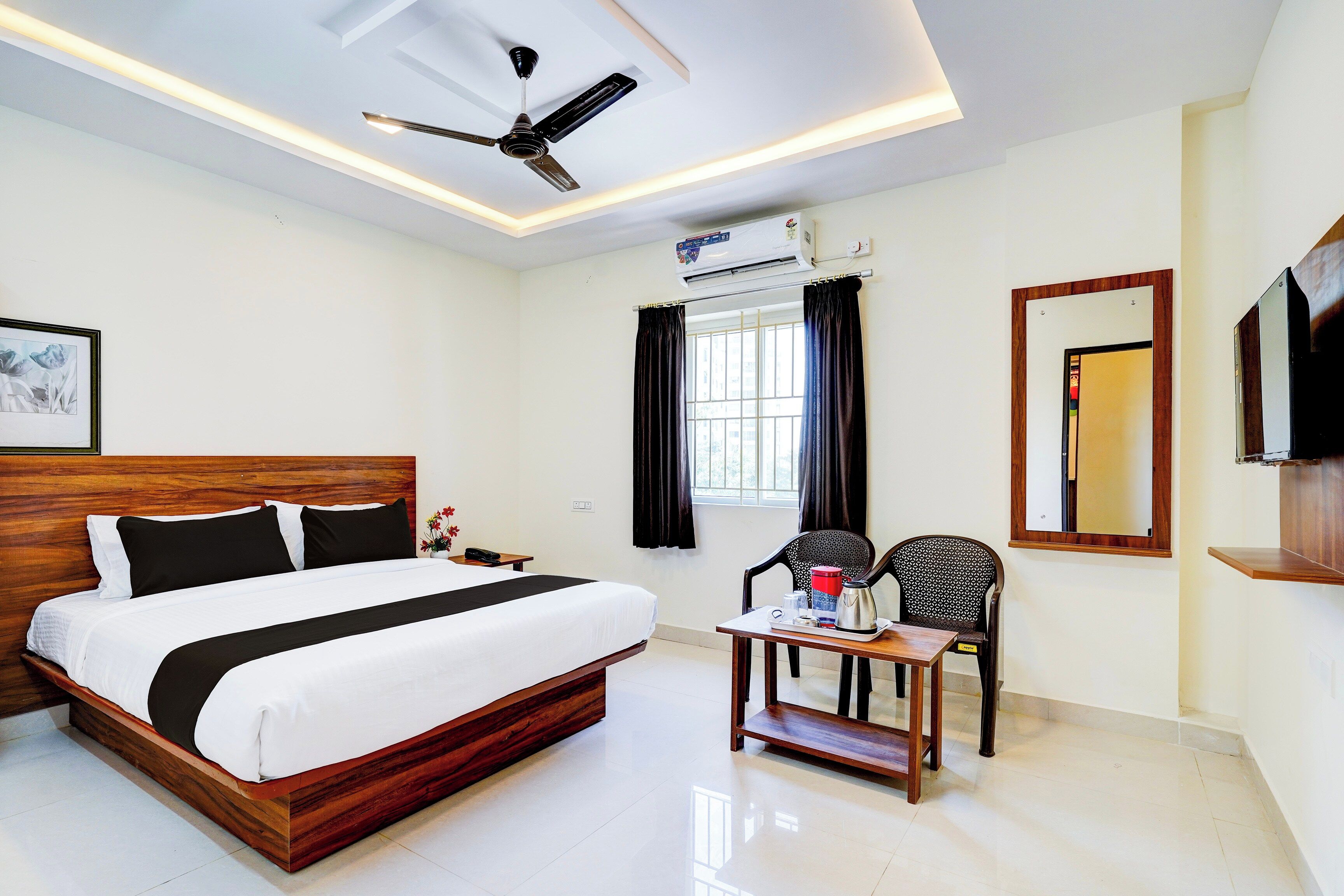 A hotel room with a bed, a desk with a chair, a ceiling fan, an air conditioning unit, and a television.