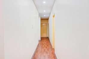 Un estrecho pasillo con suelo de madera y paredes blancas, que conduce a una puerta al final.