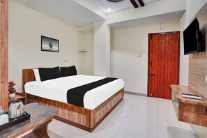 Quarto de hotel com cama, mesa de cabeceira de madeira, televisão e porta.