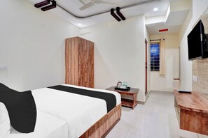 Quarto de hotel com cama, guarda-roupa de madeira, mesinha com bandeja, televisão e janela com cortinas.