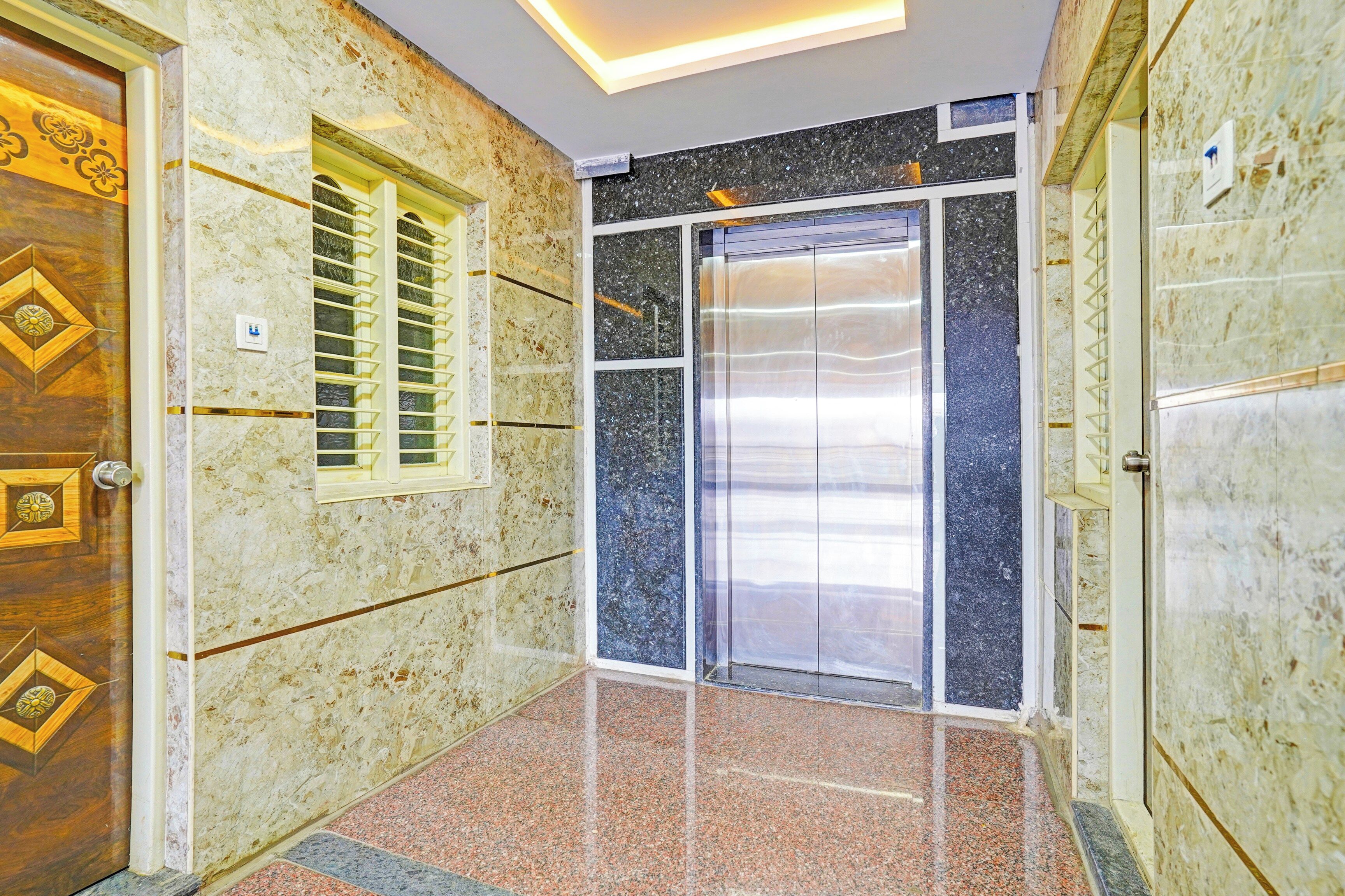 Un pasillo con puerta de madera, ascensor de vidrio y pared de mármol.