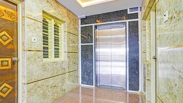 Un pasillo con puerta de madera, ascensor de vidrio y pared de mármol.