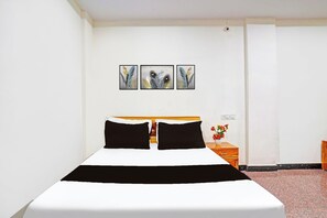 Hotellihuone, jossa on sänky, yöpöytä ja seinään kiinnitetty pistorasia.