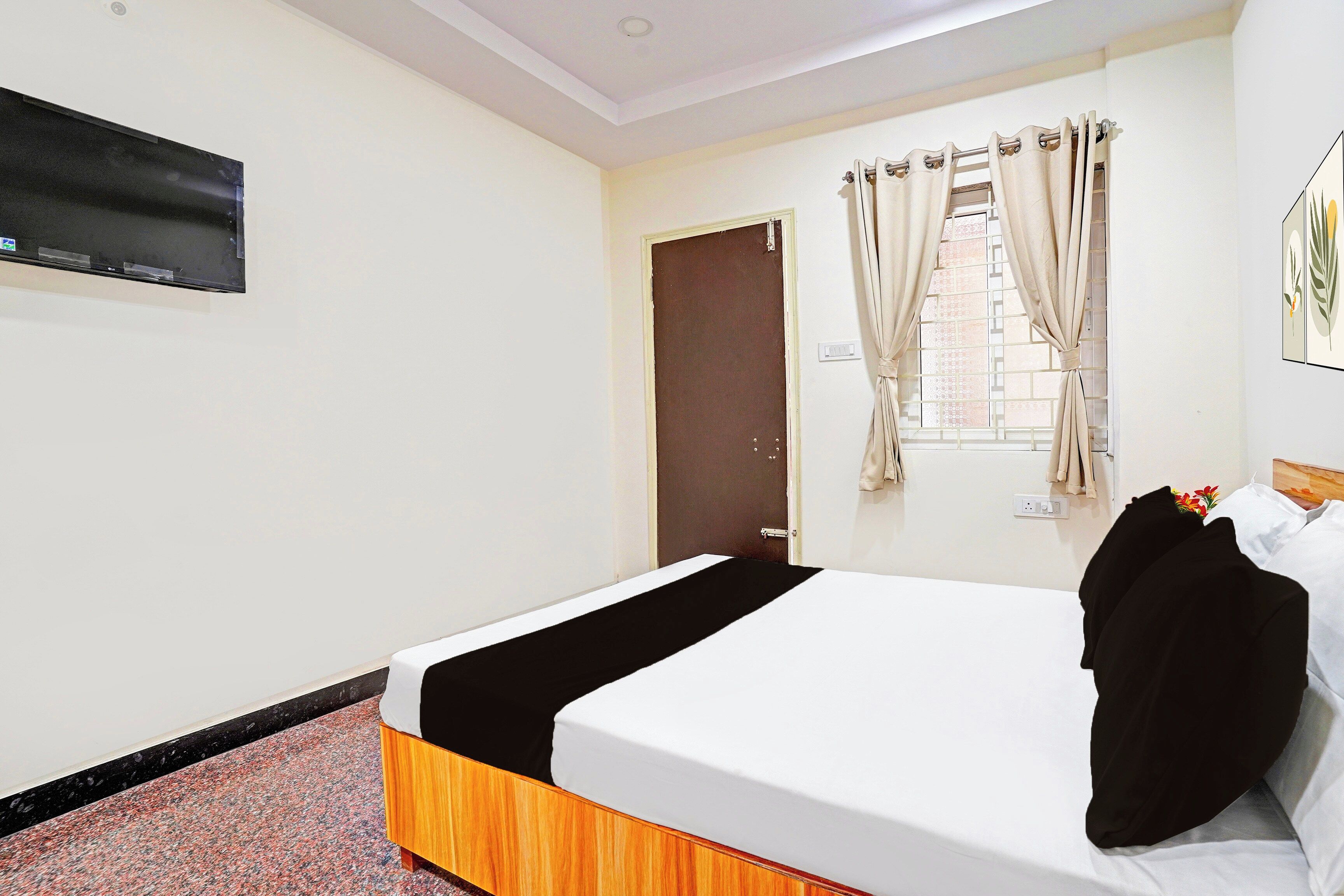 A hotel room with a bed, a television mounted on the wall, a door, and a window with curtains.