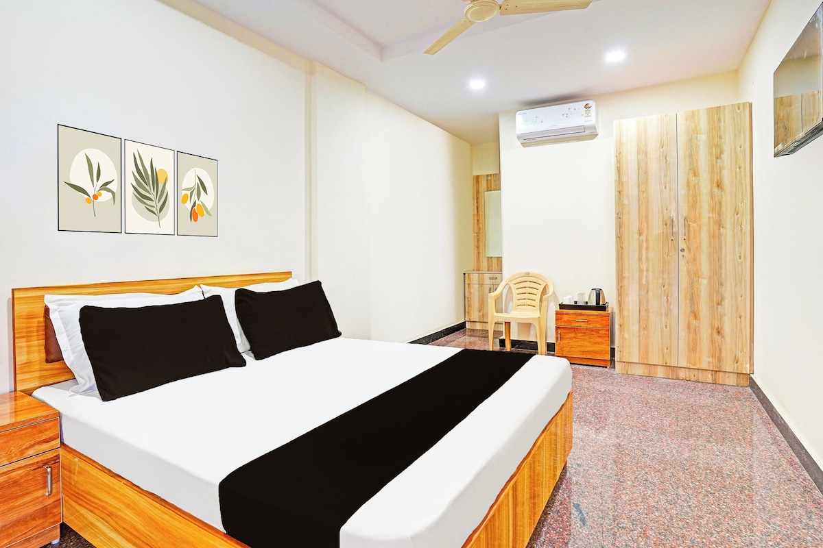 Una habitación de hotel con una cama, un armario de madera, una silla, un escritorio y obras de arte colgadas en la pared.