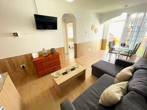 A modern living room with a flat-screen TV mounted on the wall, a wooden cabinet, a coffee table, and a sofa. - 🌟 CASA MIMOSA Two Bedroom Apartment Central Caleta Pool Private Roof Terrace 🌟 (Castillo Caleta de Fuste)