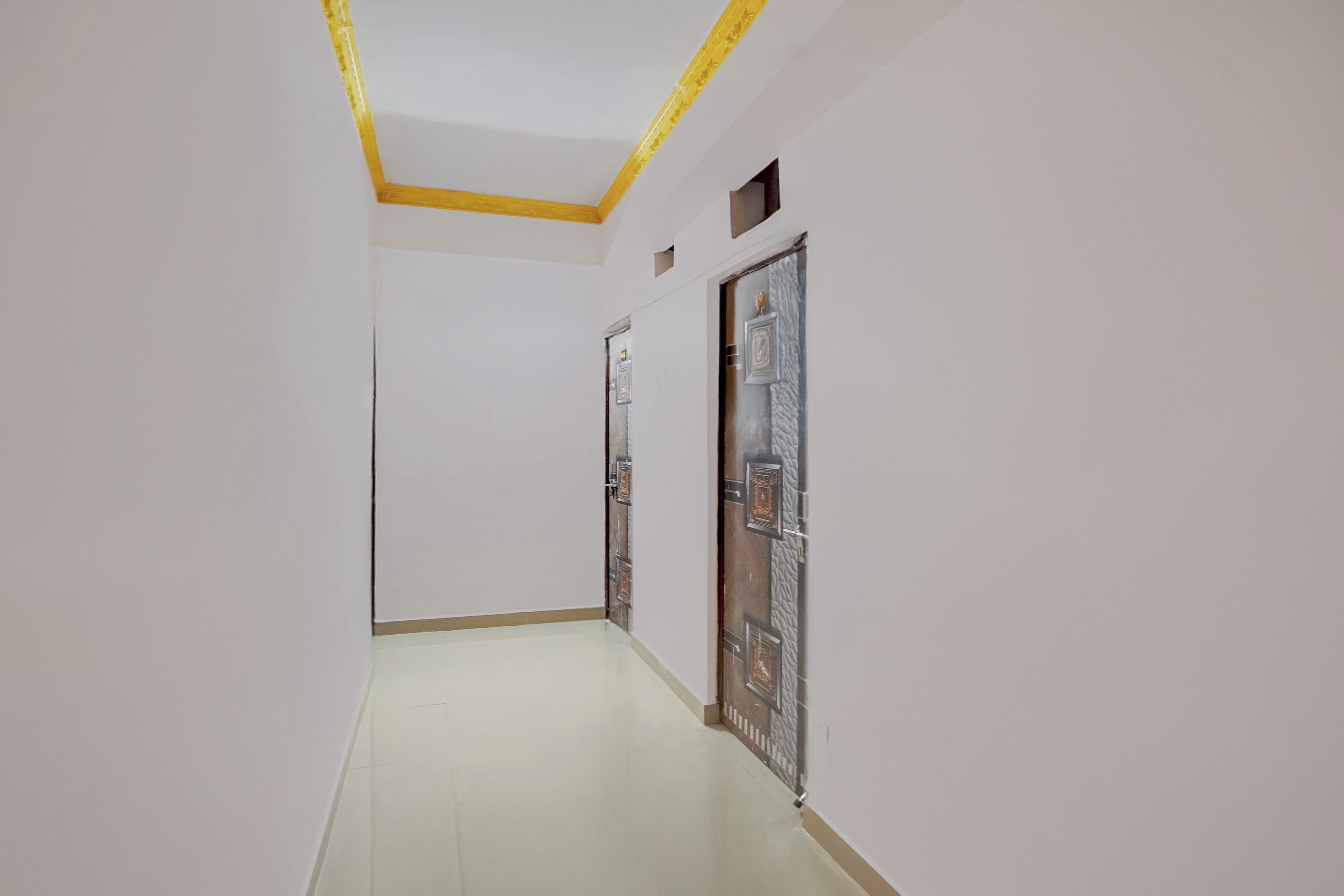 A corridor with white walls and a tiled floor, leading to a door with decorative metalwork.