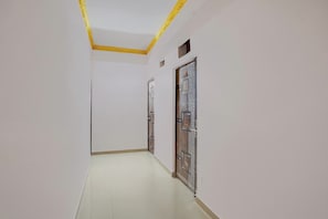 Un pasillo con paredes blancas y suelo de baldosas, que conduce a una puerta con detalles de metal decorativo.