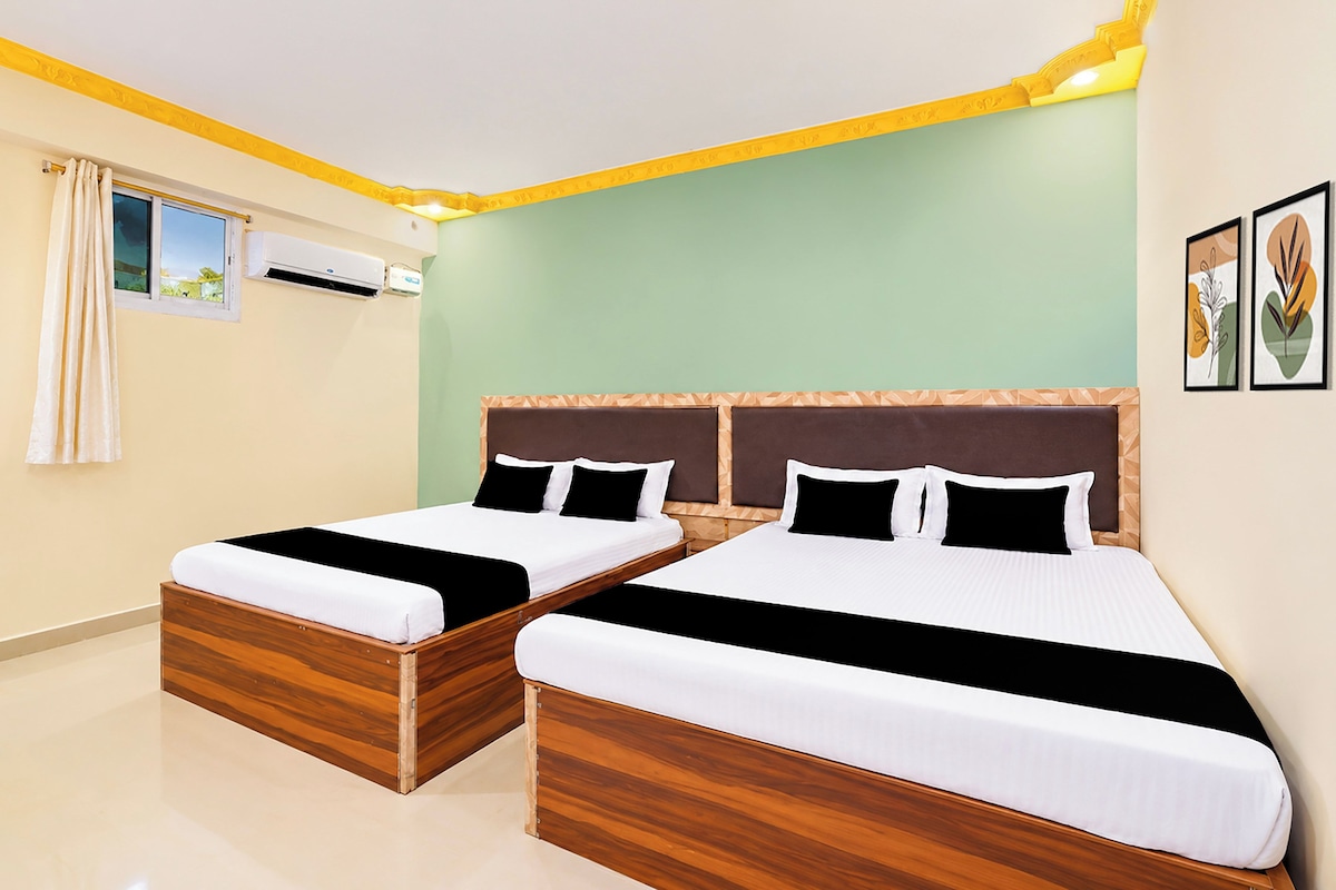 A hotel room with two beds, a window with curtains, an air conditioning unit, and framed artwork on the wall.