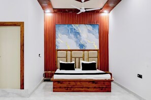 Un dormitorio con cama, ventilador de techo, un cuadro abstracto grande y cabecera de madera.