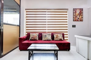 Una habitación con un sofá rojo, una mesa metálica y un ventanal con persianas horizontales.