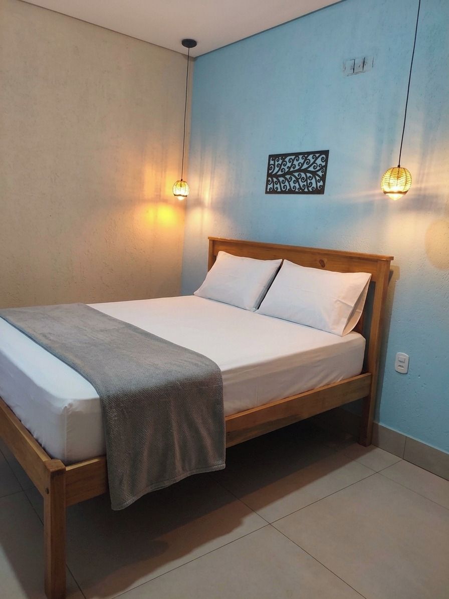 A bed with a wooden frame, white bedding, and a gray throw blanket. There are two wall-mounted light fixtures and a wall art piece.