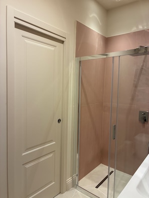 Ein Badezimmer mit Duschkabine aus Glas, einer weißen Tür und einer gefliesten Wand.