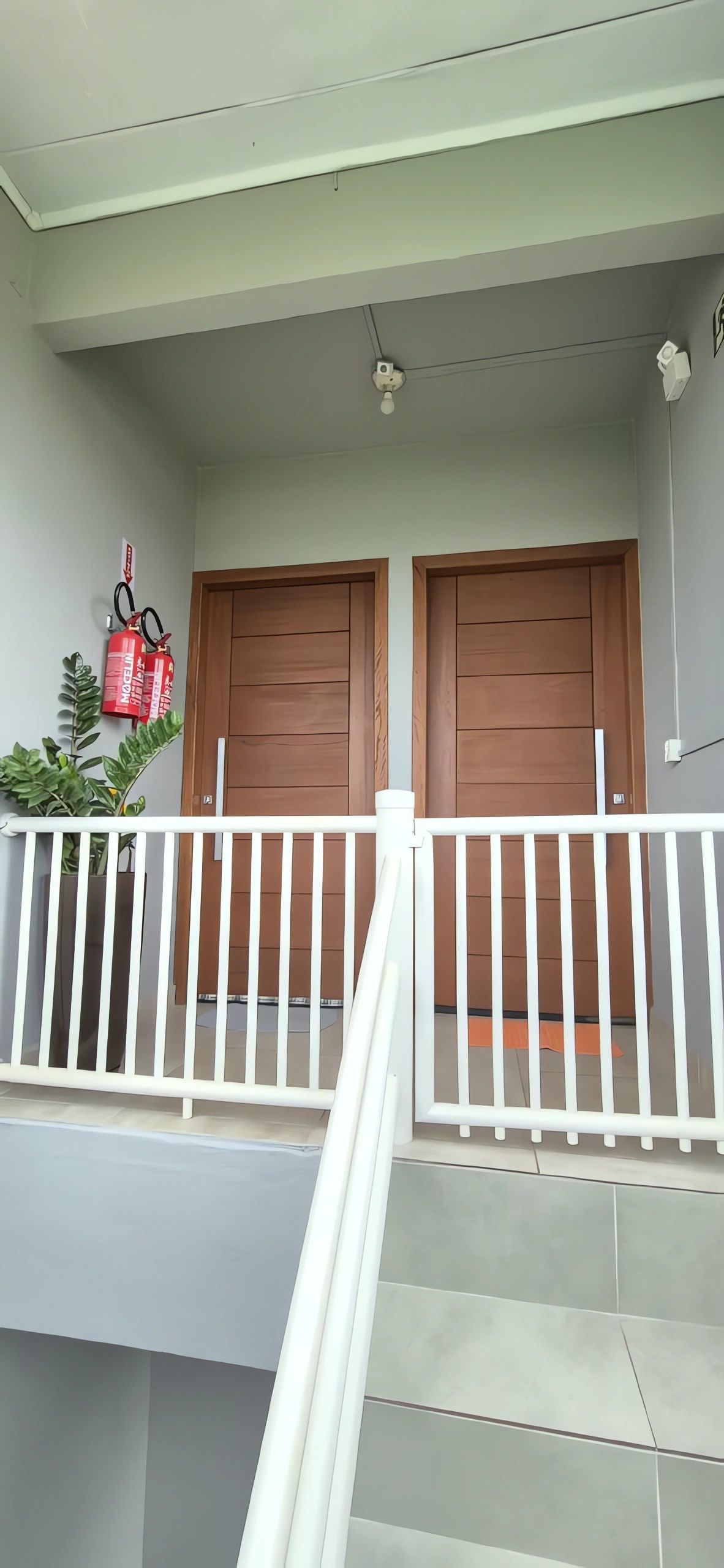 Un immeuble résidentiel doté de deux portes en bois, d’une rambarde blanche et d’un extincteur fixé au mur.