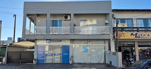 Ein zweistöckiges Gebäude mit einem Balkon, einem Laden mit einem Schild und einem parkenden Auto.