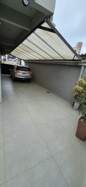 Ein überdachter Parkbereich mit einem geparkten Auto, gefliestem Boden und Topfpflanzen.